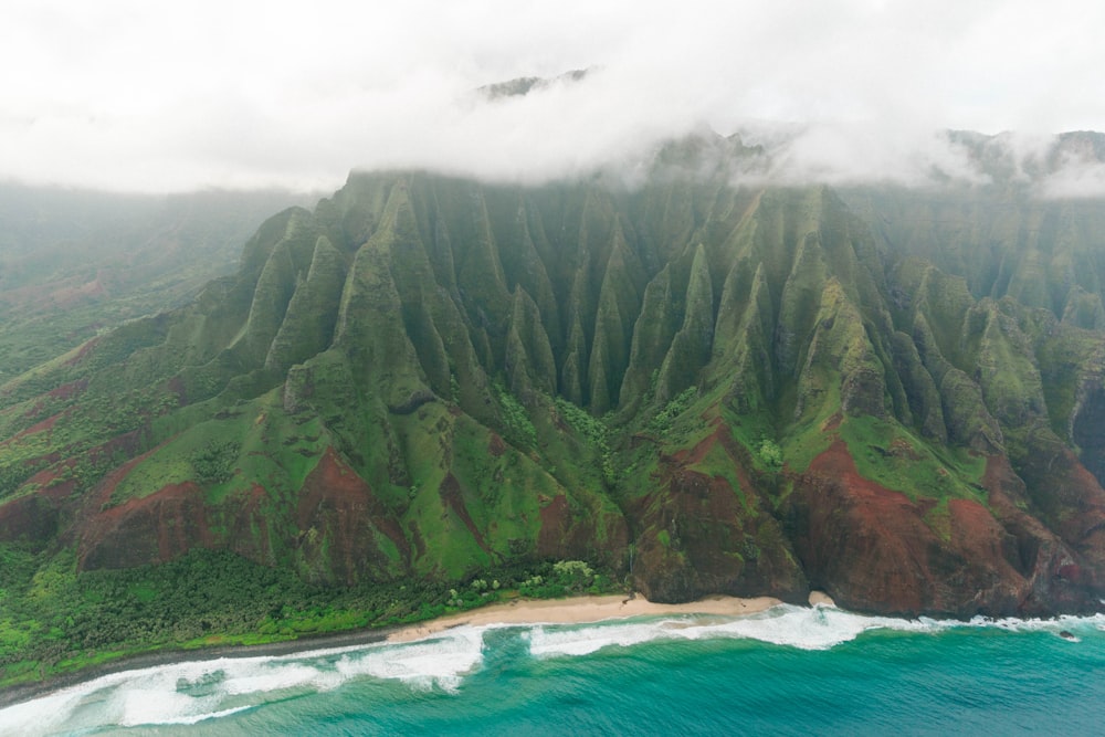 green and brown mountain beside blue sea under white clouds during daytime