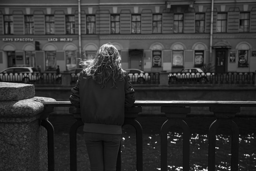 grayscale photo of woman in black coat standing near table