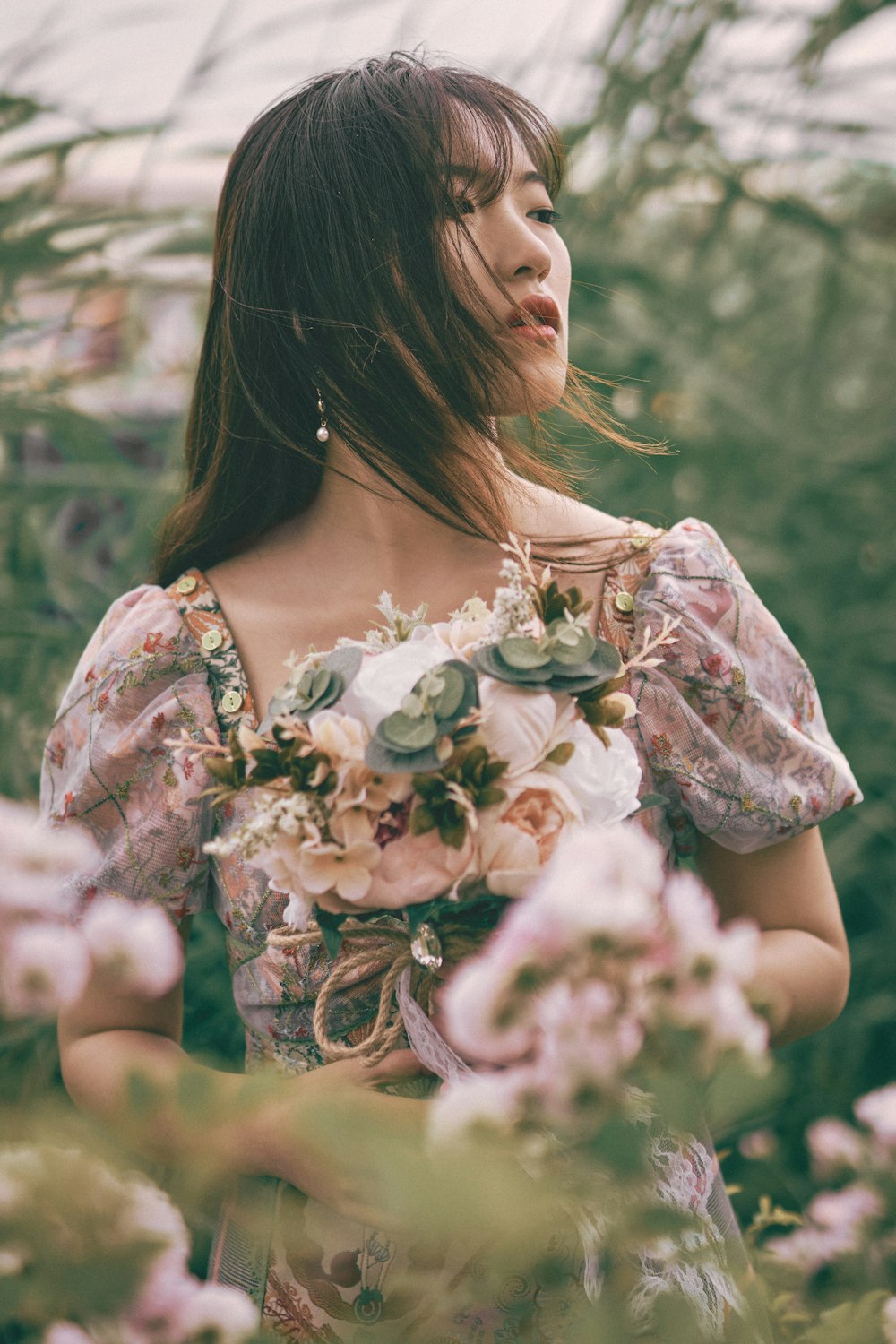 Femme en robe blanche à fleurs tenant un bouquet de fleurs