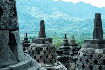 Large stone stupas with intricate patterns are set against a backdrop of lush green hills and mountains, capturing the essence of ancient cultural architecture.