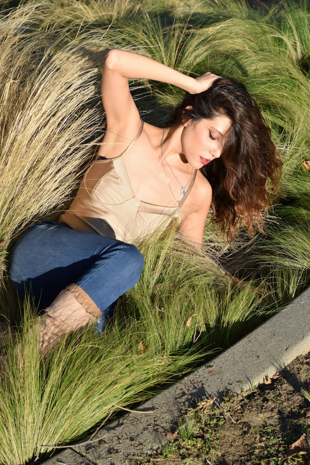 woman in beige spaghetti strap top and blue denim jeans sitting on gray concrete bench