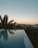 A serene infinity pool overlooking a lush tropical jungle at sunset.