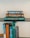 A collection of books is stacked neatly on two levels of a glass shelf. On the top shelf, three books are stacked horizontally. The titles include 'Starfarers' by Poul Anderson, 'All Cloudless Glory,' and 'U.S. Battleships.' The spines of additional books can be seen on the bottom level, including titles like 'AMBRA' and '1993 Directory of Members.' The books have varied colored covers, mostly in blue, green, and brown tones.