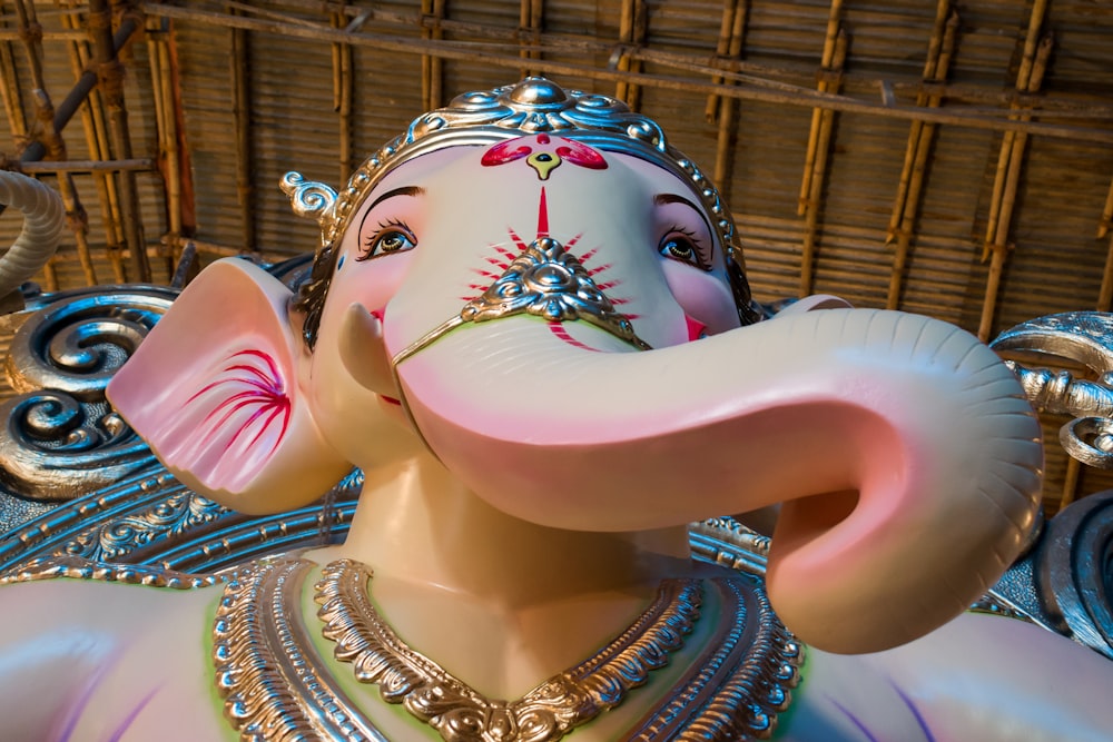 mujer en vestido de sari dorado y rojo sosteniendo una figura de elefante rosa