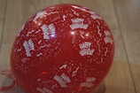 A red balloon featuring white text and patterns, including the phrase 'Happy Birthday' and festive confetti and streamers, set against a wooden floor.