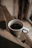 A close-up of a bright ceramic mug filled with steaming coffee, resting on a wooden table with soft morning light.