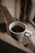 A close-up of a bright ceramic mug filled with steaming coffee, resting on a wooden table with soft morning light.
