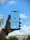 A hand is holding a smartphone in front of a blue sky with clouds. The phone screen shows an airplane flying directly overhead, creating an illusion that the plane is part of the sky view.