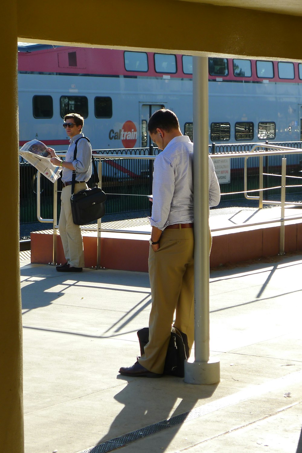 man in gray dress shirt and brown pants standing beside blue metal railings during daytime