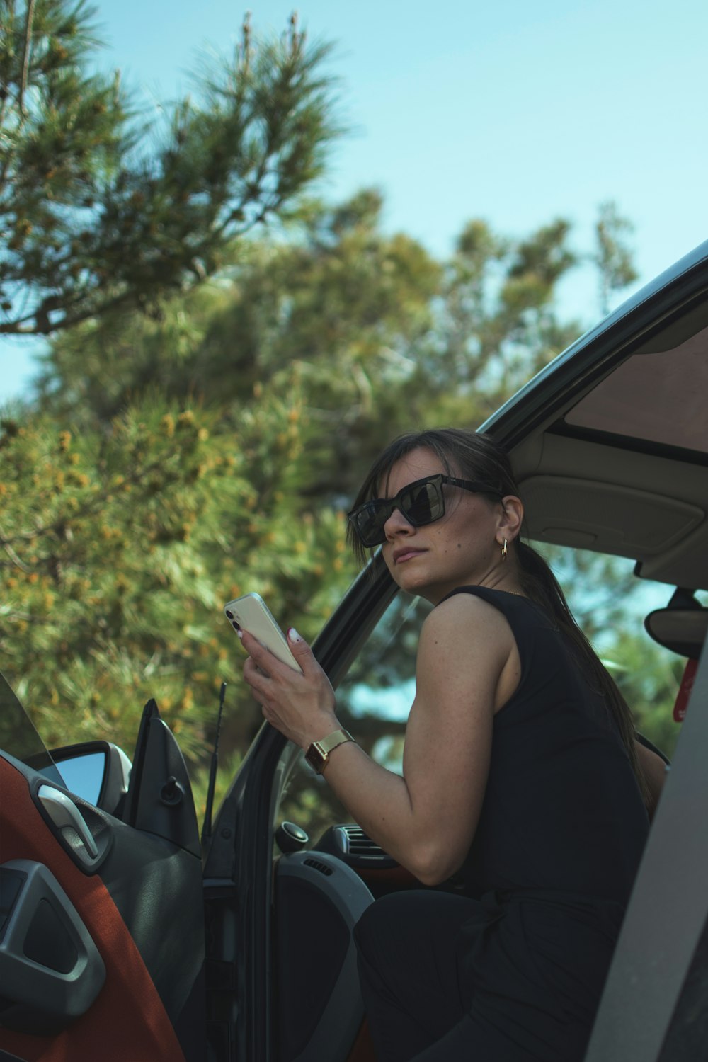 mulher na regata preta que veste óculos de sol pretos segurando o smartphone