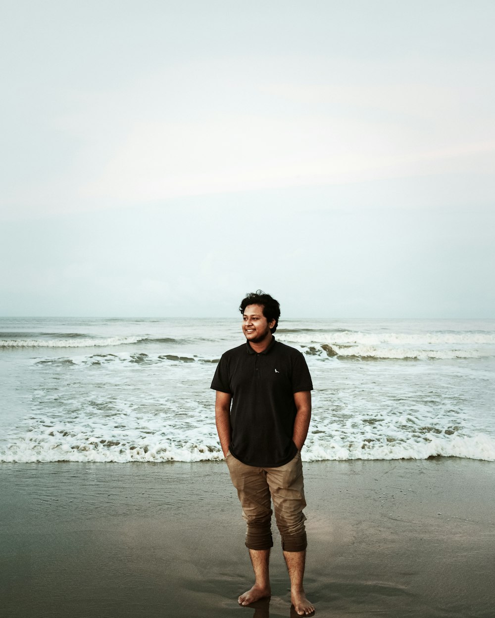 man in black crew neck t-shirt and brown pants standing on beach shore