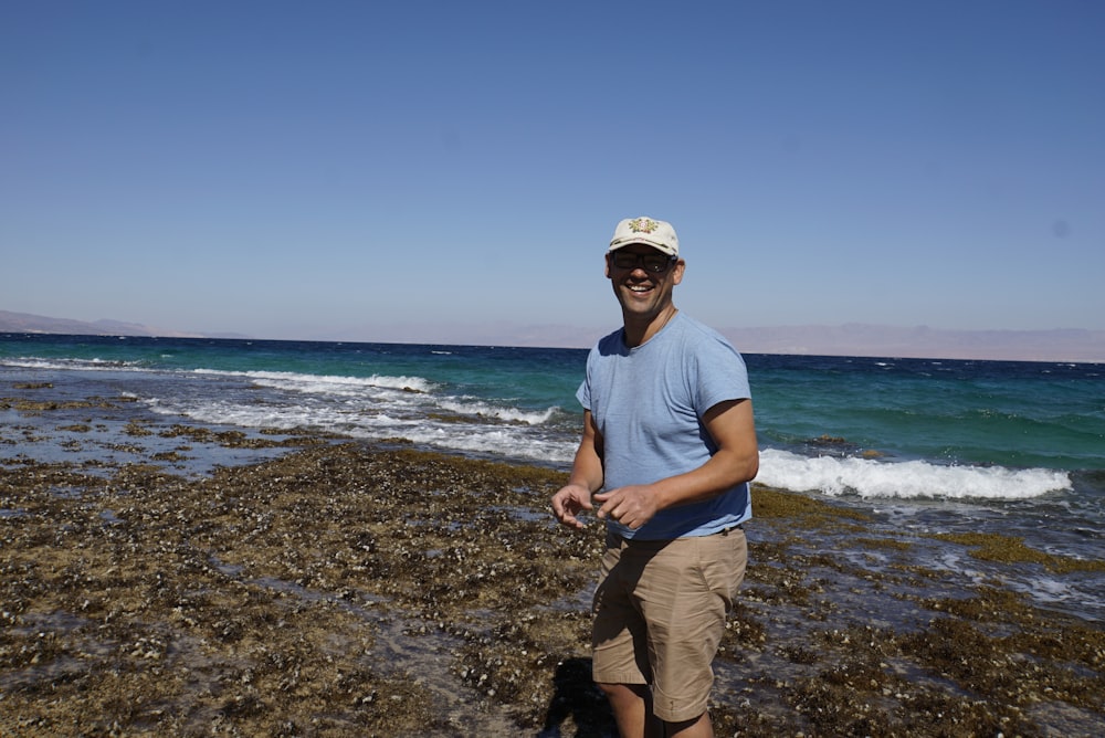 man in blue crew neck t-shirt and brown pants standing on beach during daytime