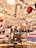 A festive store display is filled with holiday decorations, including large candy canes suspended from the ceiling, shiny red and gold balloons, and an assortment of Christmas-themed merchandise. The rich decor exudes a lively and vibrant atmosphere with colorful gift boxes and ornamented shelves.