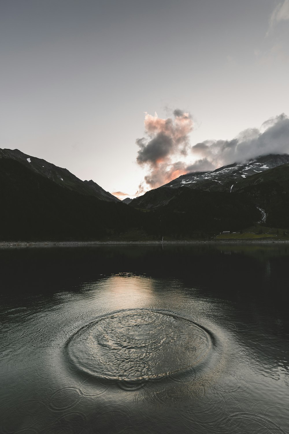 body of water near mountain under white clouds during daytime