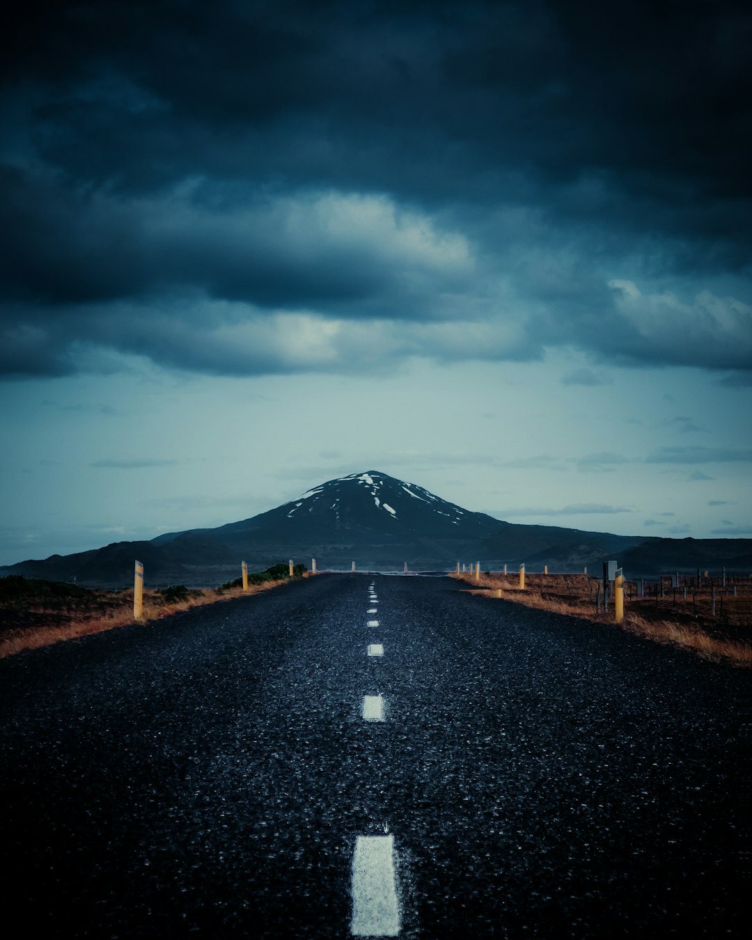 gray concrete road between brown grass field under white clouds and blue sky during daytime