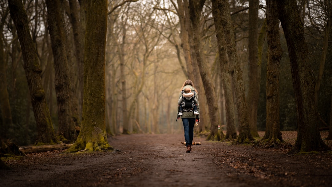 woman in black and white jacket walking on pathway between trees during daytime