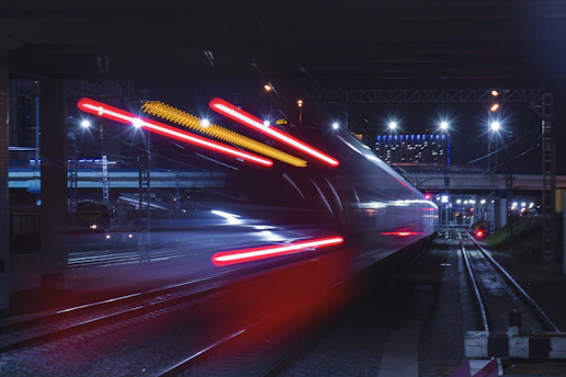 A sleek futuristic train speeding under glowing neon city lights at dusk.
