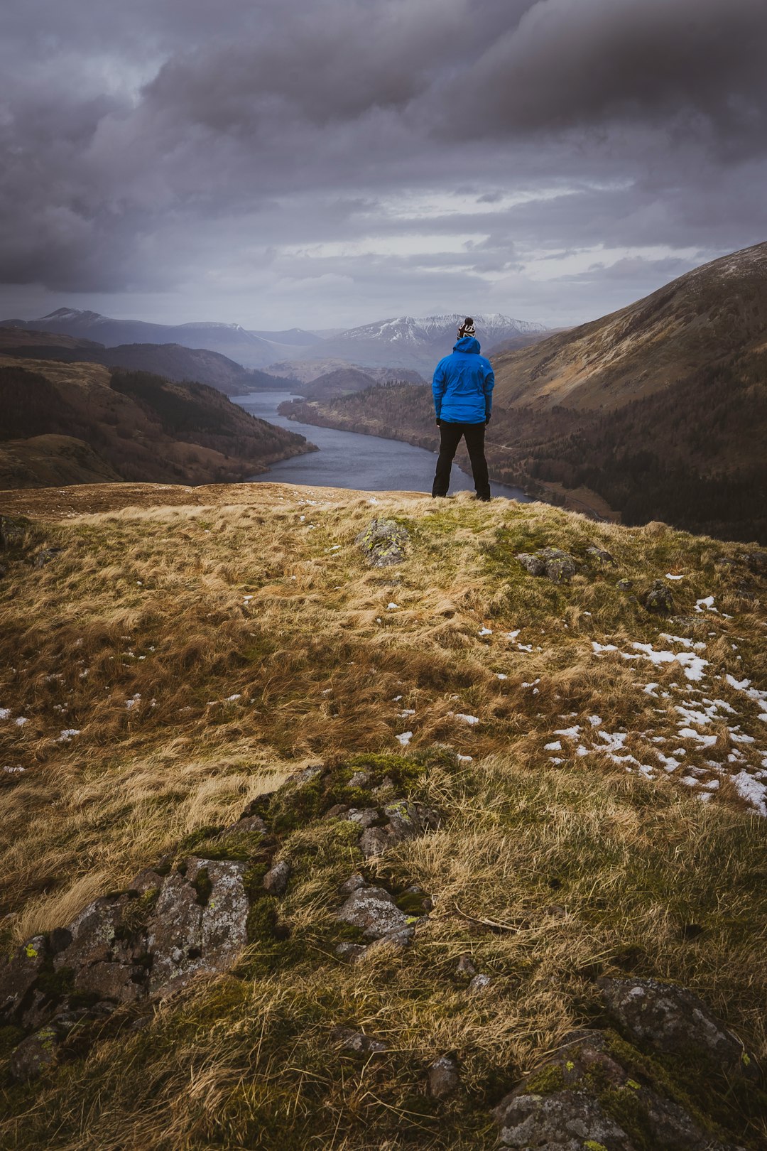 person in blue jacket standing on brown and green mountain during daytime