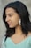 A woman with dark hair and a pleasant smile is captured in profile view. She is wearing a pair of distinctive shell earrings and a light blue, patterned top featuring floral accents.