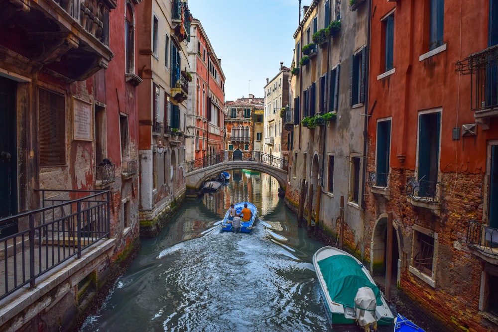 blue boat on river between brown concrete buildings during daytime