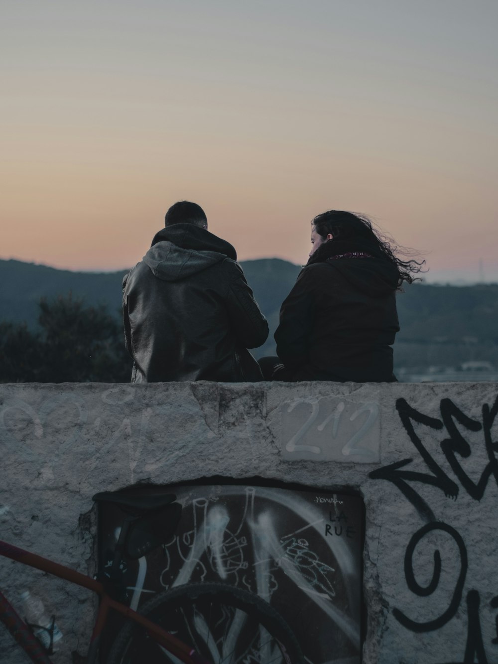 2 person sitting on concrete fence near body of water during daytime