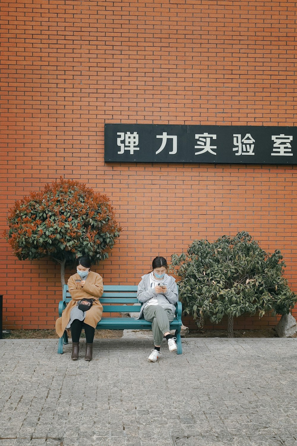 2 men sitting on bench near red brick wall