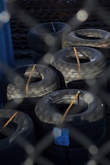 Stacks of heavy-duty tires are secured with straps, positioned on a surface surrounded by metal fencing. The tires have a rugged appearance, suggesting they might be used for commercial or industrial purposes.