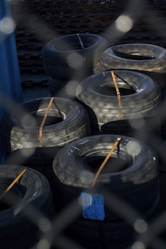 Stacks of heavy-duty tires are secured with straps, positioned on a surface surrounded by metal fencing. The tires have a rugged appearance, suggesting they might be used for commercial or industrial purposes.