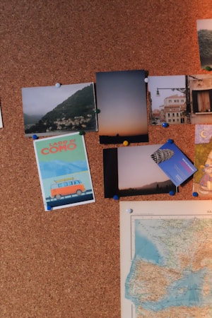A corkboard with various pinned items including photographs, postcards, and a map. The photos depict scenic landscapes, city streets, and an illustration of a van with the text 'Lago di Como'. The map shows a section of what appears to be Europe. It is organized with colored push pins holding everything in place.