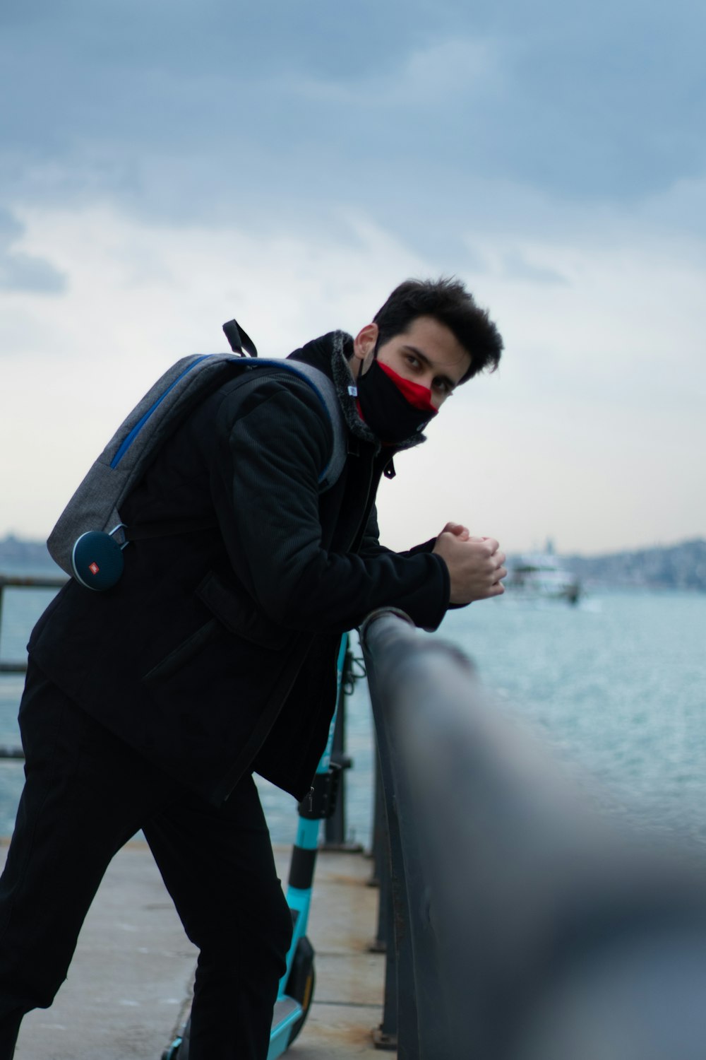 Mann in schwarzer Jacke und schwarzer Hose trägt schwarzen Rucksack, der tagsüber auf dem Boot steht