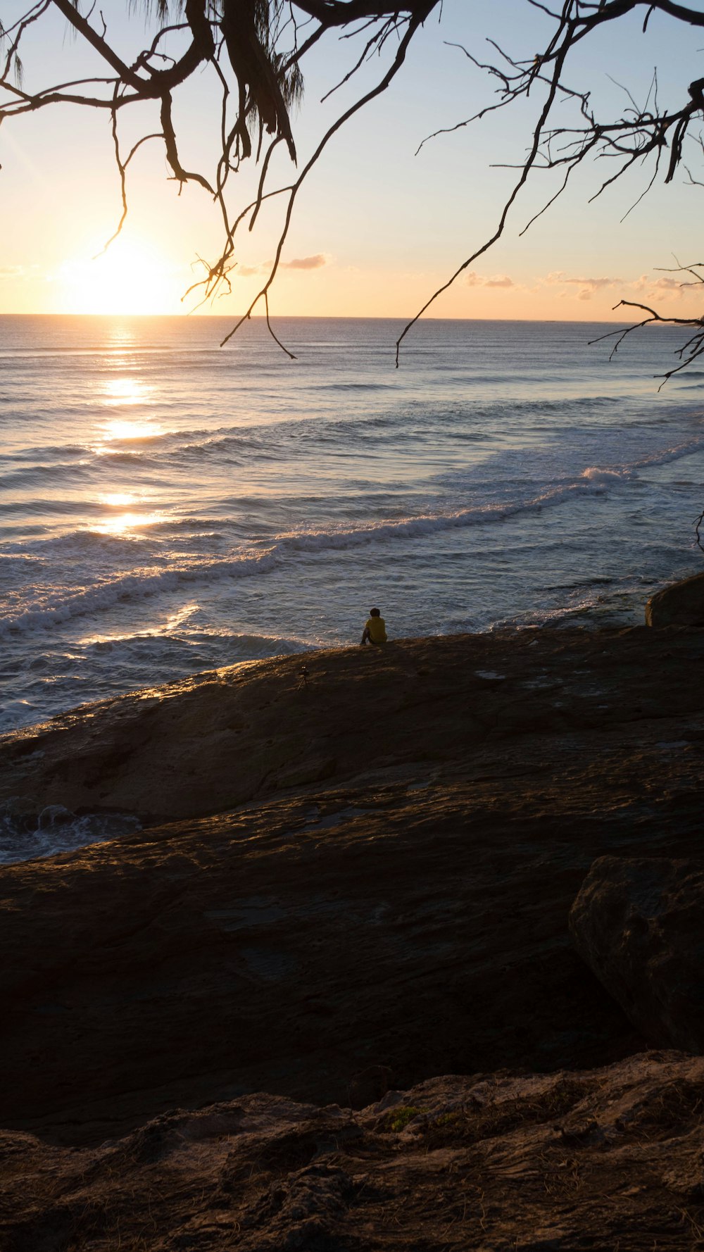 Person, die tagsüber auf einem Felsen in der Nähe des Meeres sitzt