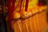 A collection of yellow bobblehead toys with smiling faces and red tassels attached. The toys are arranged in a row, each with a spring connecting the head and base. The background is blurred but features similar toys, creating a repetitive pattern.