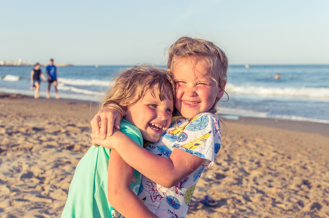 two children with blonde hair hugging each other happily on the beach