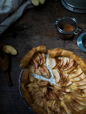 Close-up photo of a golden-brown apple tart with cinnamon sprinkled on top, served on a rustic wooden table.