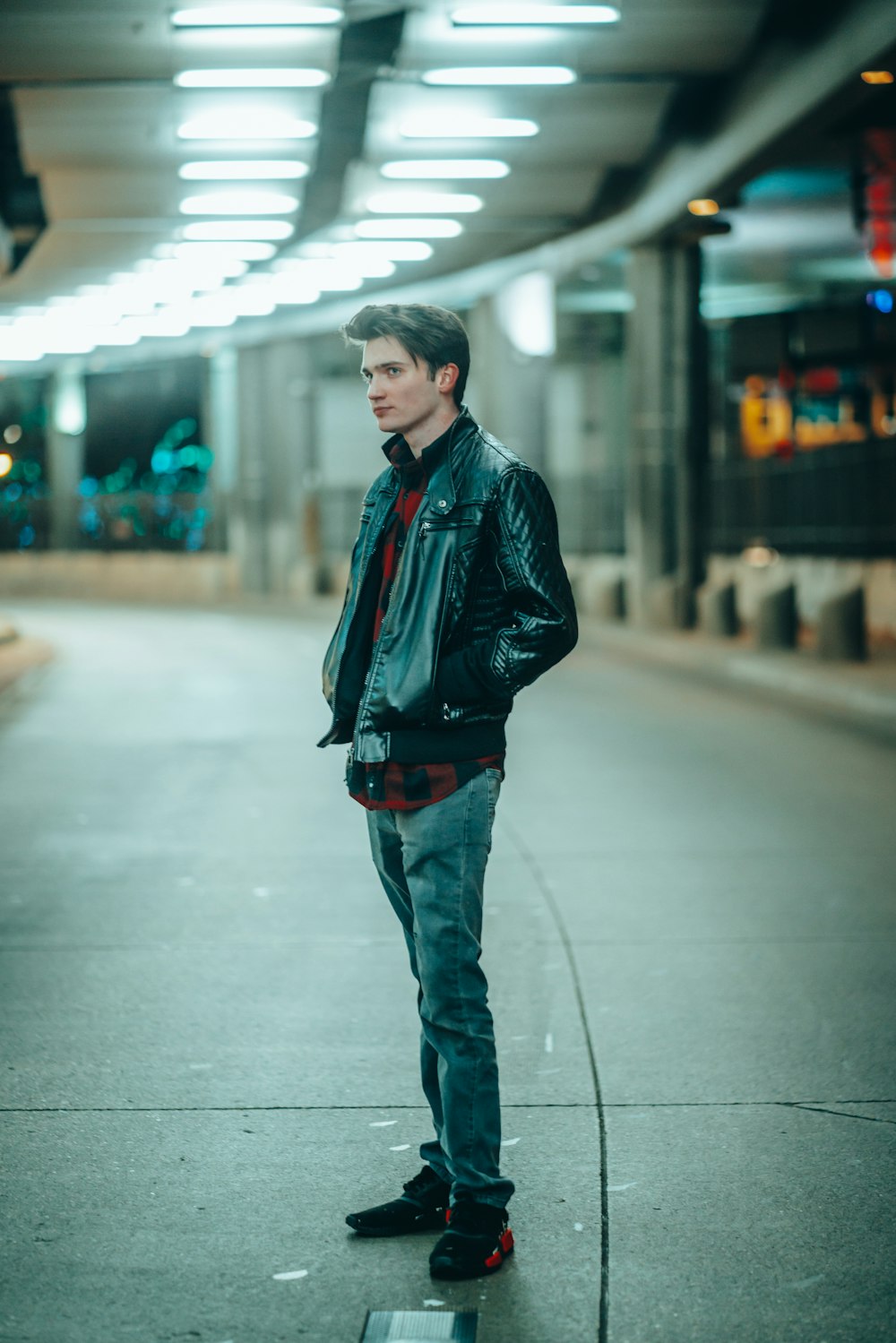 man in black leather jacket standing on sidewalk during daytime