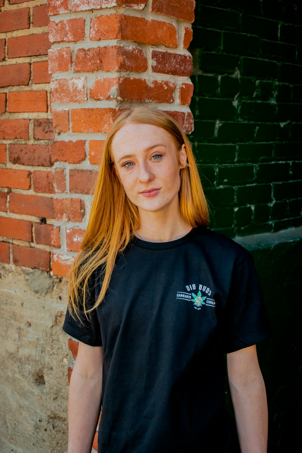 woman in black crew neck t-shirt standing beside brown brick wall