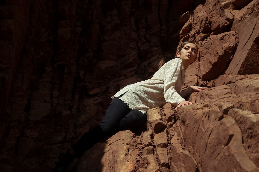 man in white sweater and blue denim jeans sitting on brown rock