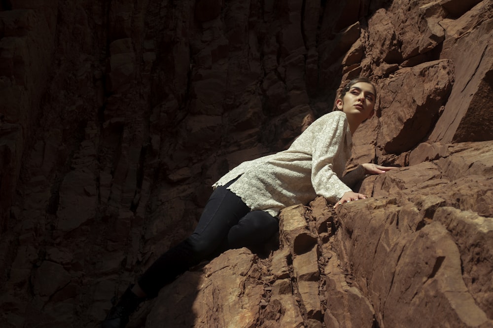 man in white sweater and blue denim jeans sitting on brown rock