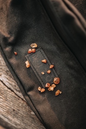 A collection of small, amber-colored crystals scattered on a dark fabric surface. The fabric appears textured, possibly part of a bag or clothing. The crystals are irregularly shaped and vary in size, adding a natural element to the scene.