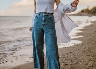 woman in white tank top and blue denim jeans standing on beach during daytime
