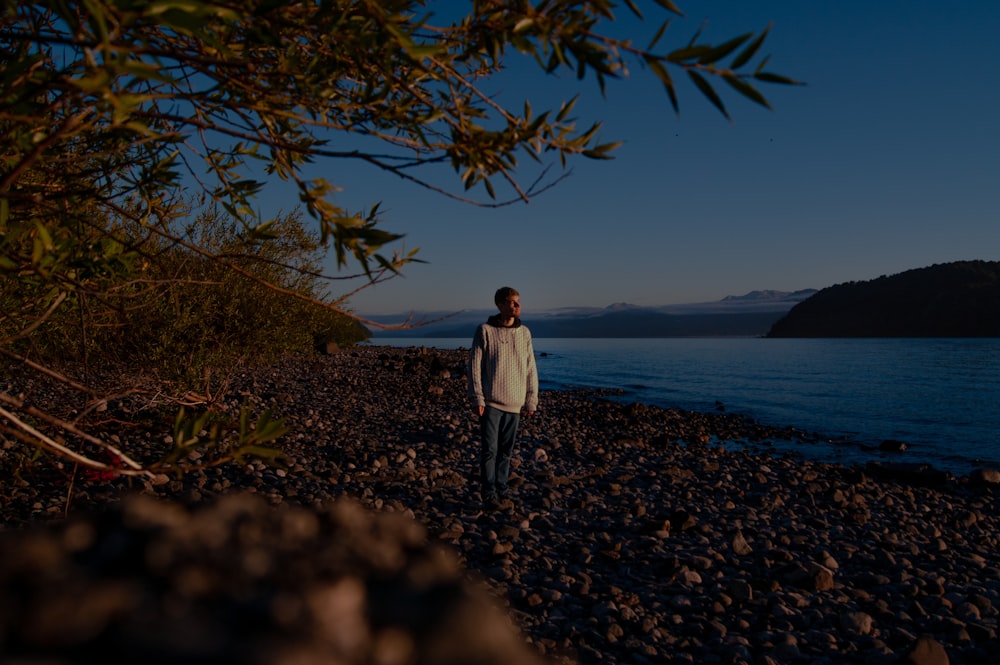 woman in white long sleeve shirt standing on brown soil near body of water during daytime