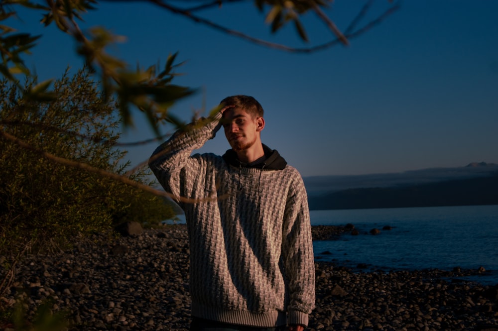 man in brown and black sweater standing on brown sand near body of water during daytime