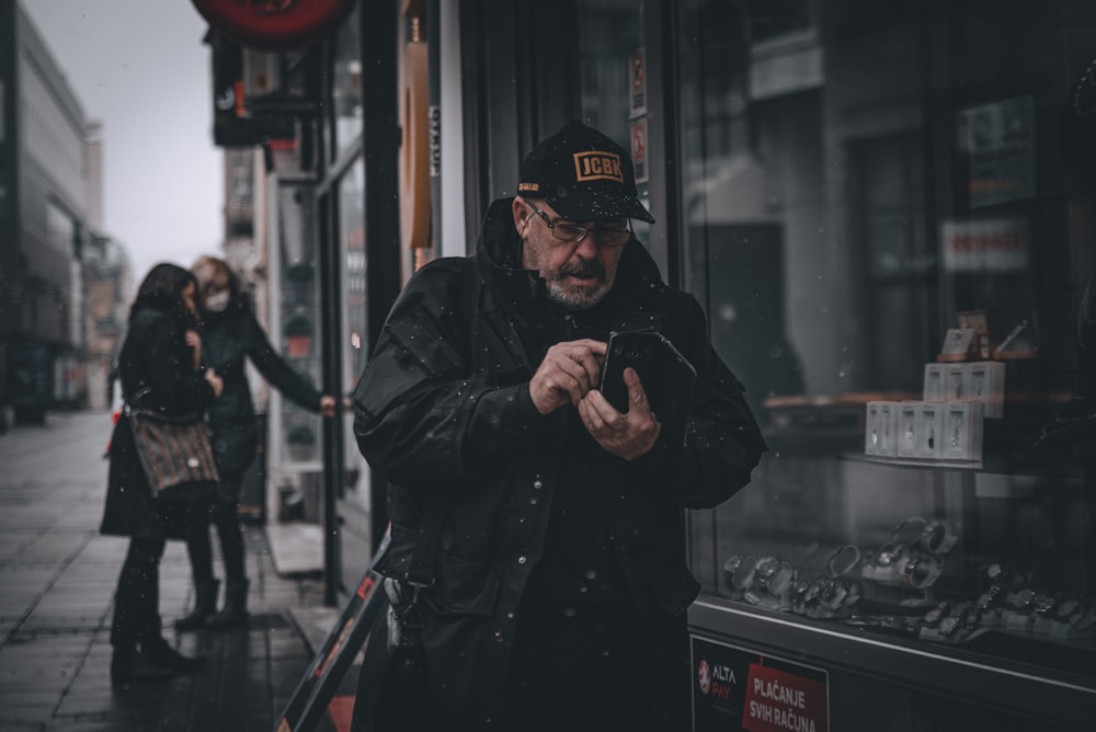 man in black jacket and black cap standing near glass window