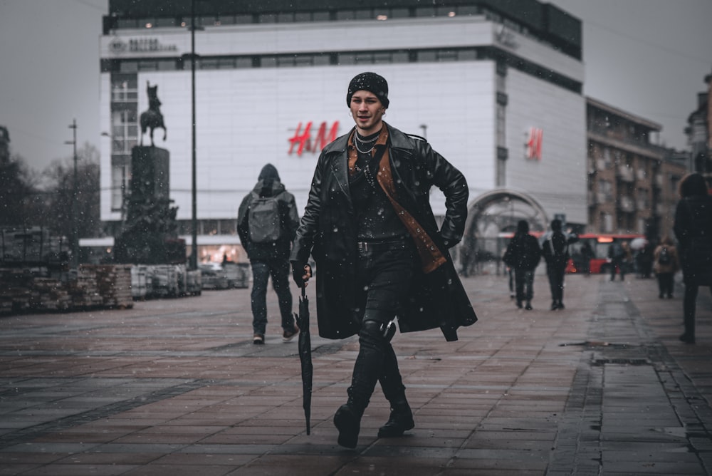 man in black leather jacket standing on sidewalk during daytime