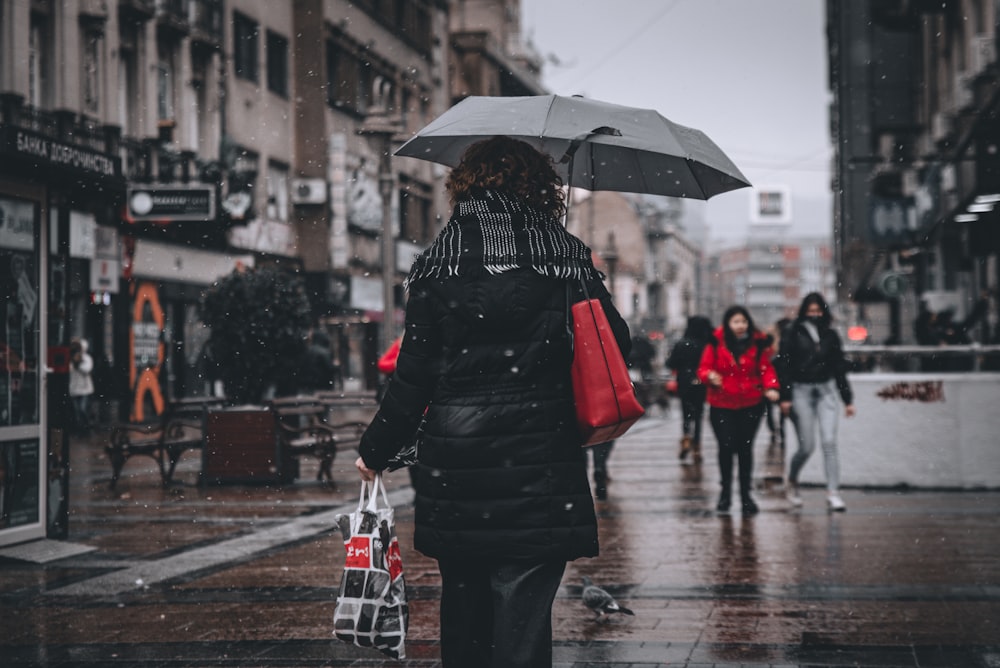woman in black and white polka dot coat holding umbrella walking on street during daytime