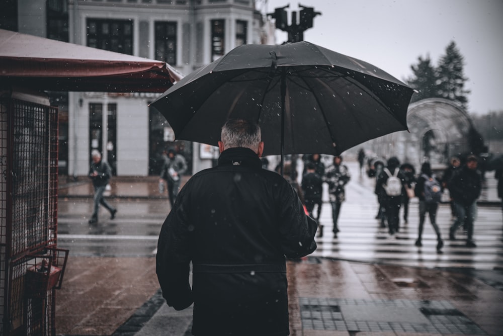 man in black coat holding umbrella walking on sidewalk during daytime