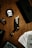 A tactical knife with intricate designs is placed on a wooden surface. Surrounding it are playing cards, a black ring, and black circular coasters featuring a white skull and crossbones symbol. The setup is complemented by a black box also adorned with the skull motif.