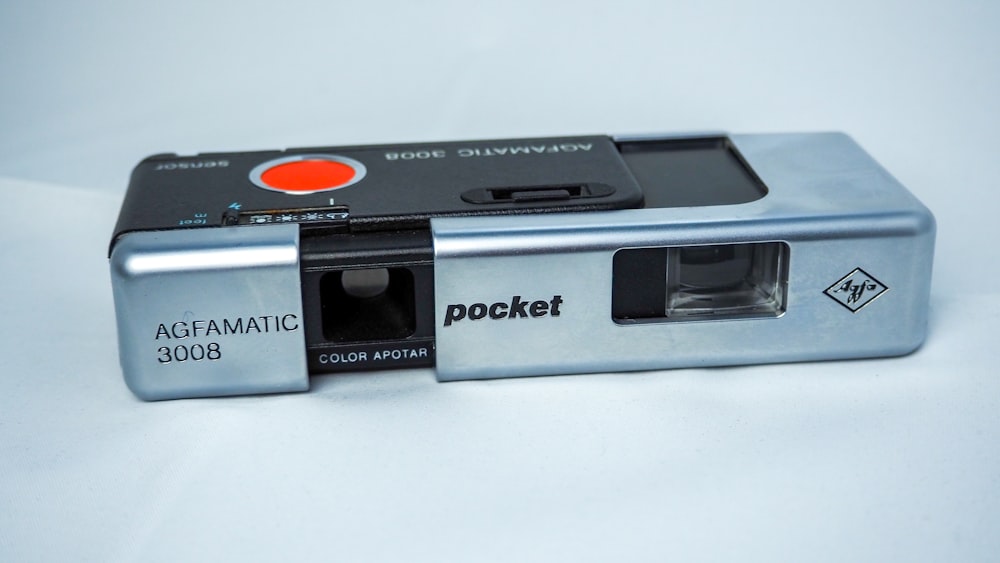 a silver camera with a red button on it