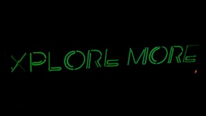 Neon green text on a black background reads 'XPLORE MORE', emitting a glowing effect.
