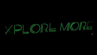 Neon green text on a black background reads 'XPLORE MORE', emitting a glowing effect.